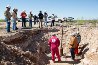 Contractors and attorneys for Chevron watch from above as Hawk Dunlap, Daniel Charest and Sarah Stogner (from left) inspect an excavated well on April 10 at Antina Ranch in Crane County, Texas. Credit: Mitch Borden/Marfa Public Radio