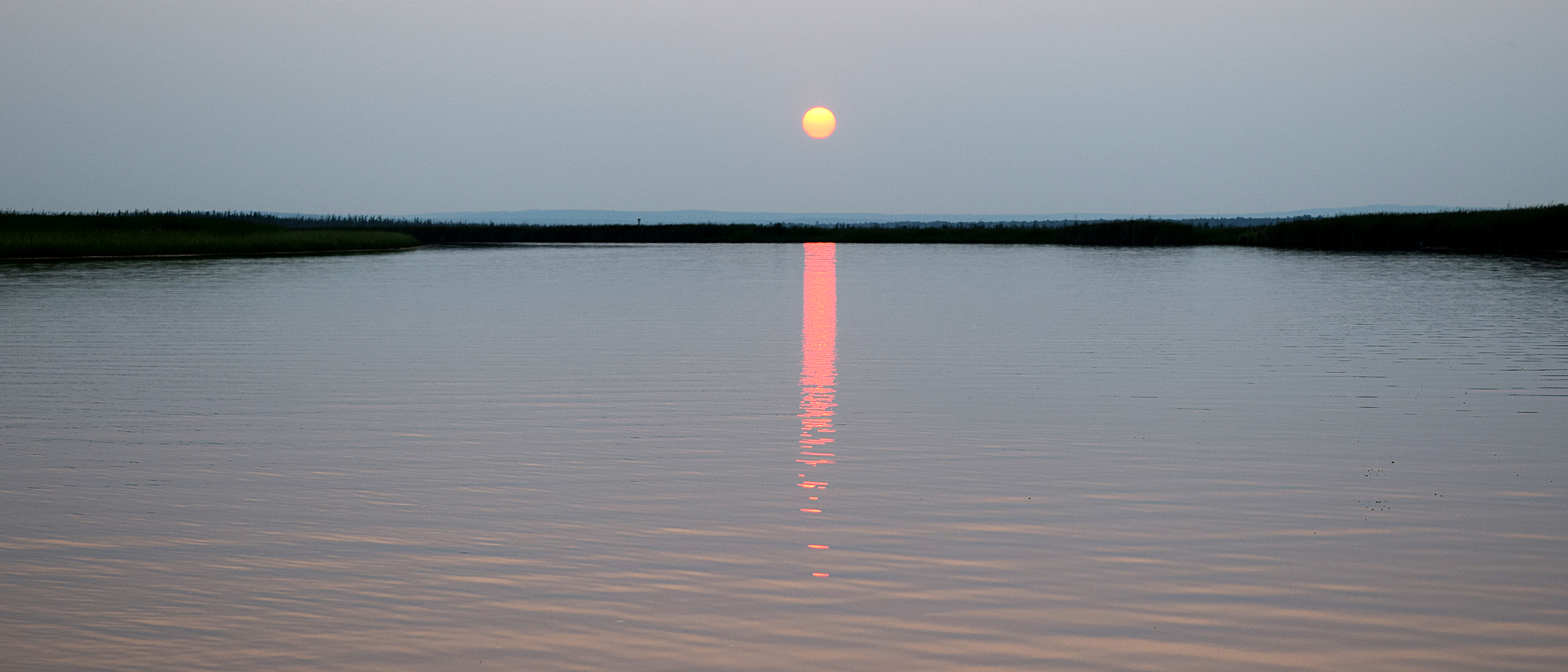 The sun reflects a red line into the still water