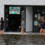 People walk through flood waters past a store with a broken window on Aug. 30, 2023 after Hurricane Idalia hit Crystal River, Fla. Credit: Joe Raedle/Getty Images