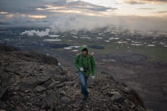 Vasily Ryabinin scales an overlook on the Taimyr Peninsula in June 2020, with the sprawl of the Norilsk Nickel complex visible below. He toured the area with Russian journalists shortly after resigning from his job with Russia's environmental protection agency due to his concern over what he saw as its failure to fully investigate the spill of 6.5 million gallons of diesel fuel into Arctic waterways last year. Credit: Yuri Kozyrev, NOOR