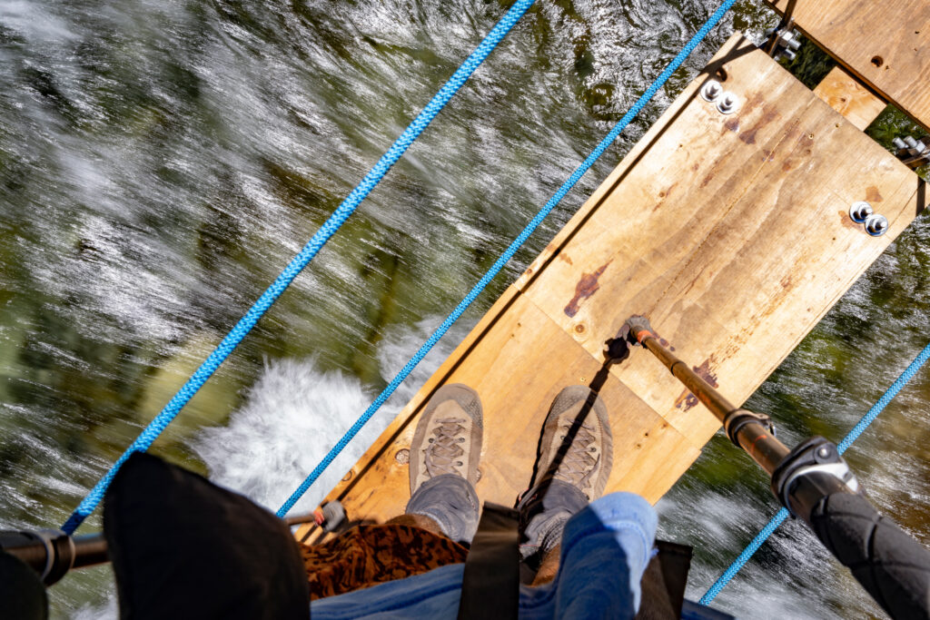 A makeshift suspension bridge rocks over the South Fork San Joaquin River in lieu of the original San Joaquin Bridge that was destroyed in the winter of 2023. A sign by the bridge warned that it was not built to regulation and for hikers to cross at their own peril. Credit: Bing Lin/Inside Climate News