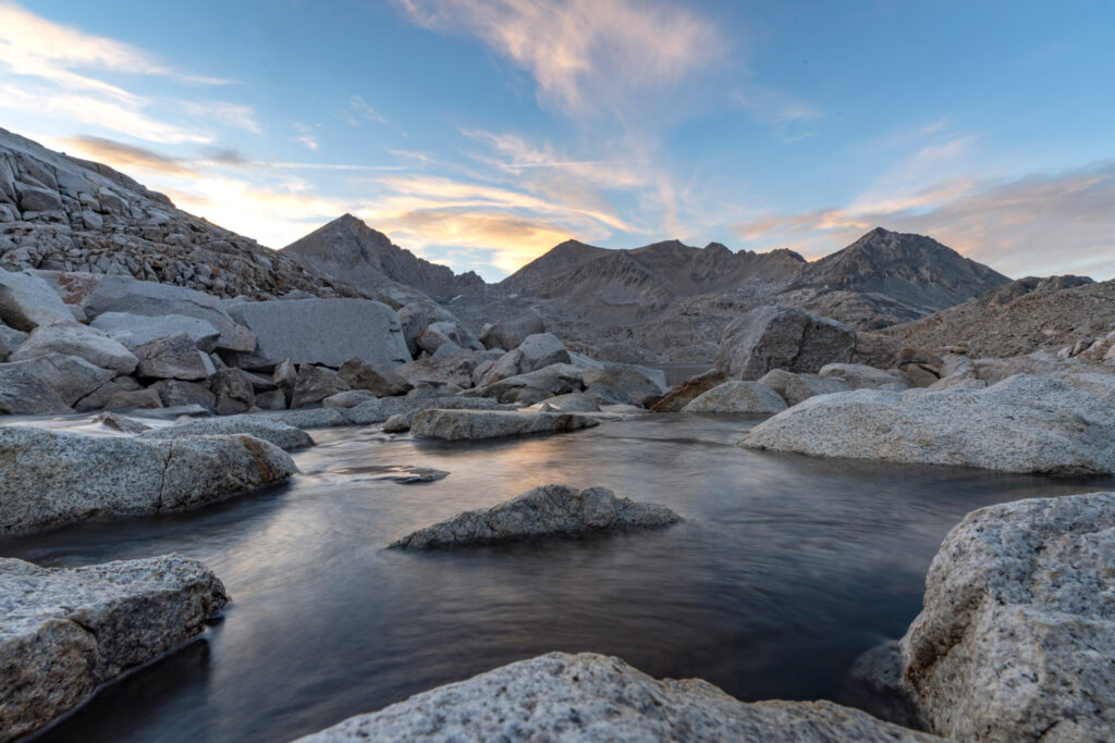 A stream flows between rocks towards mountain outcrops in the distance, just south of Muir Pass in the High Sierras at sunset. Credit: Bing Lin/Inside Climate News